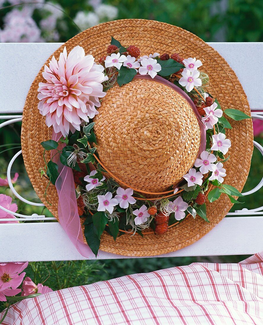 Straw hat decorated with clematis wreath on garden bench
