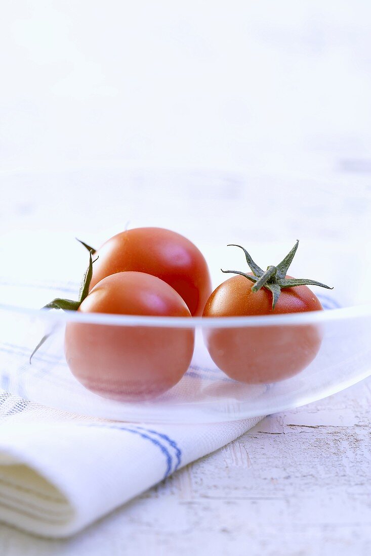 Three tomatoes in glass dish on tea towel