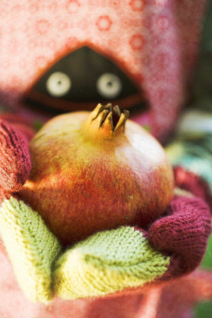 Child's hands in woollen mittens holding pomegranate