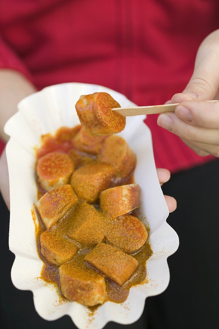 Person isst Currywurst mit Ketchup