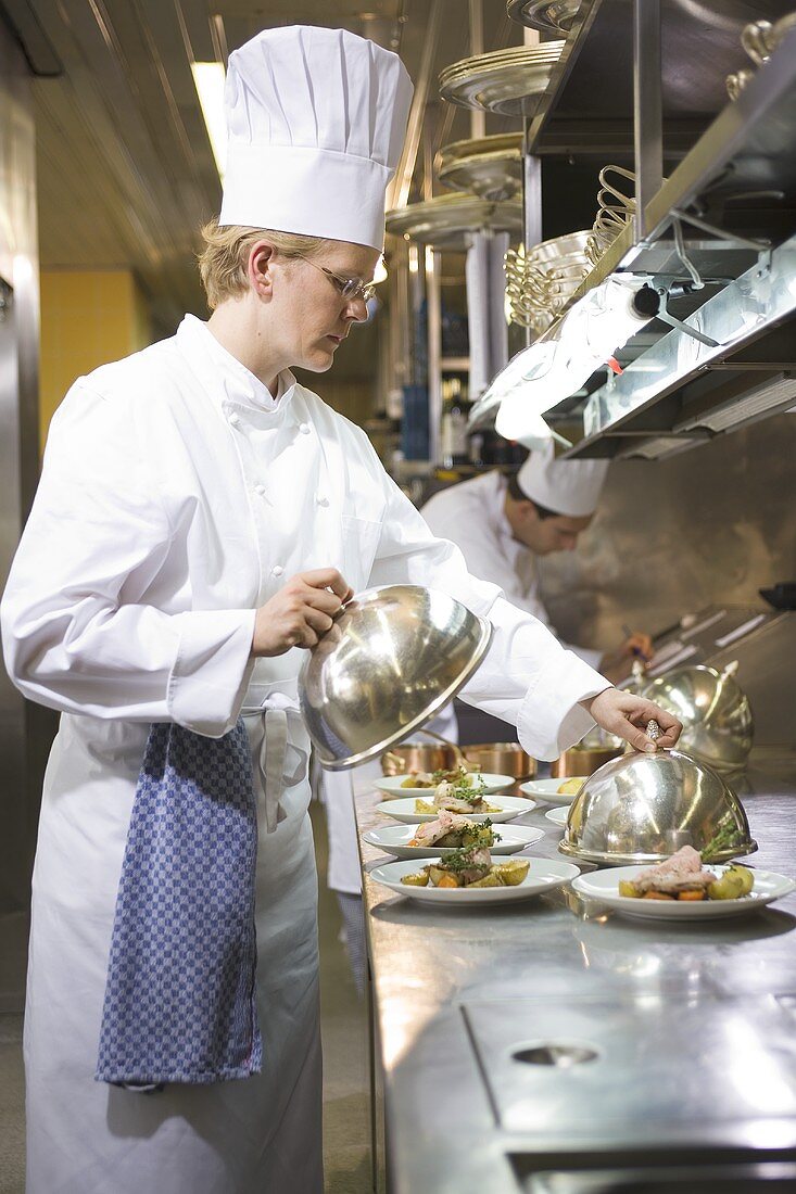 Female chef putting domed covers over main courses