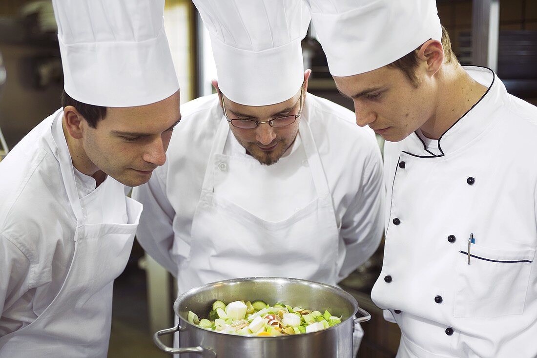 Three chefs examining the contents of a pan