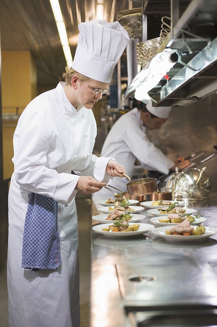 Female chef spooning sauce over main courses