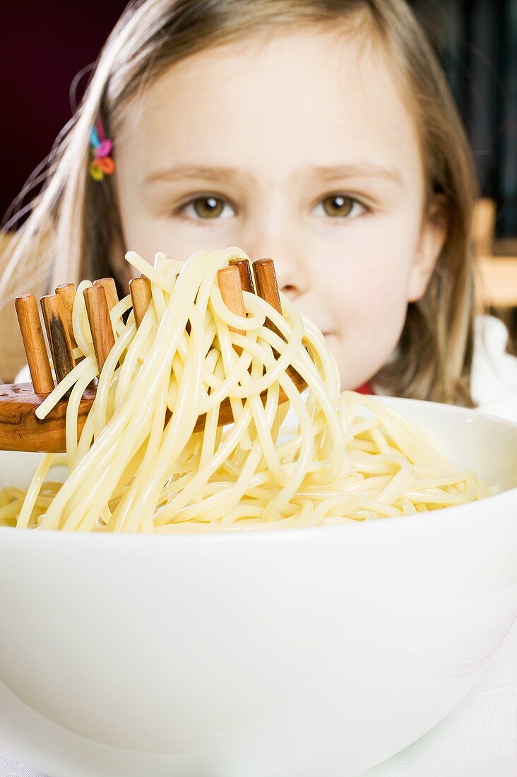 Mädchen hebt mit Spaghettiheber Nudeln aus Schüssel