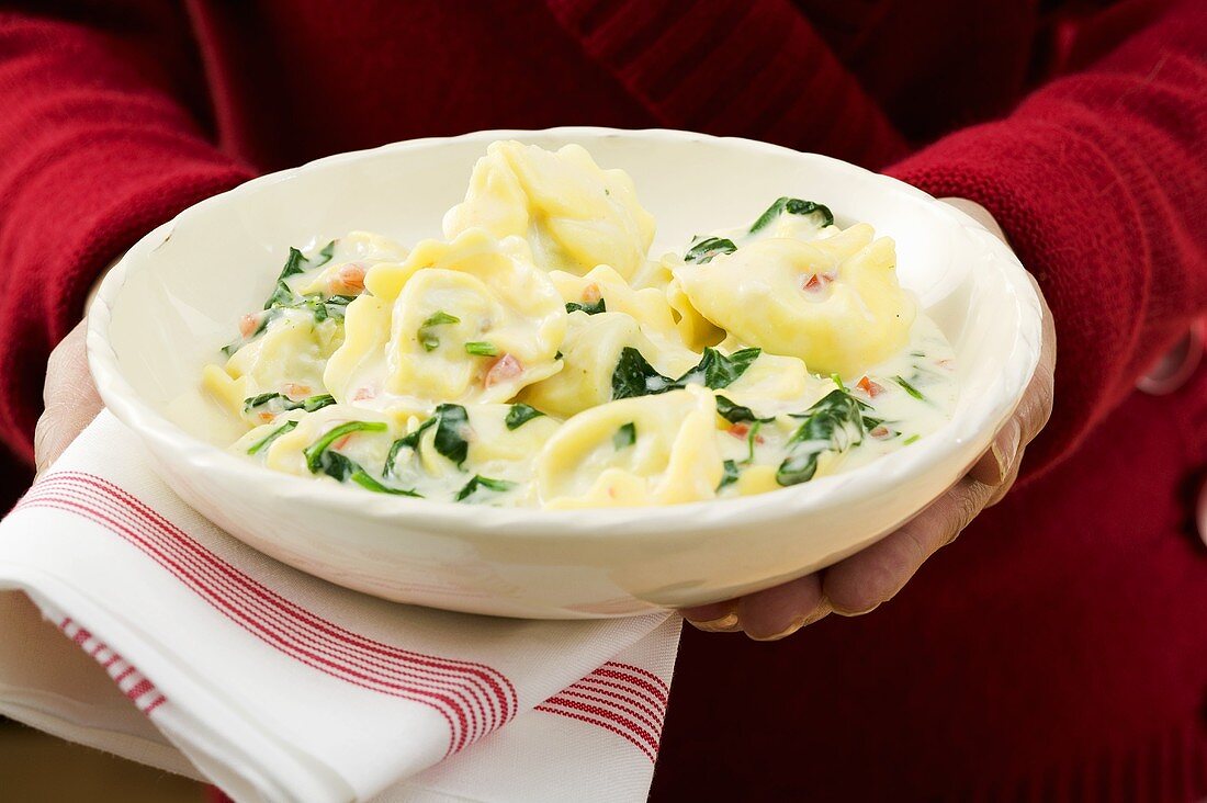 Frau hält Teller Tortellini mit Spinat und Sahnesauce