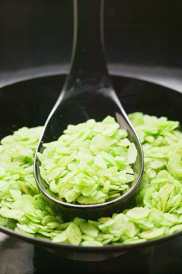 Green rice flakes (unripe rice grains) in bowl with spoon