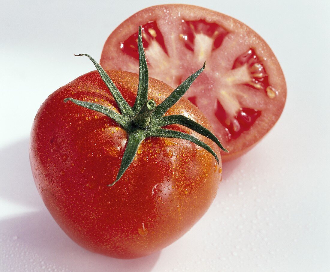 Whole and half tomato with drops of water