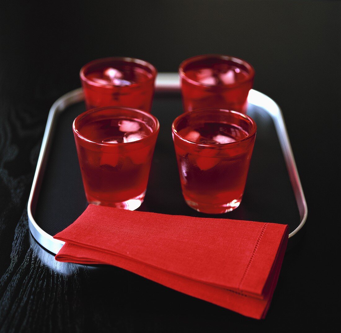 Rote Gläser mit Wasser und Eiswürfeln auf Tablett