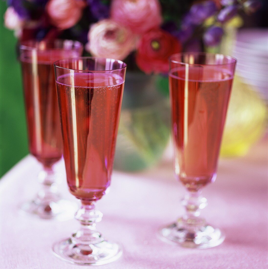 Three glasses of pink sparkling wine in front of flowers