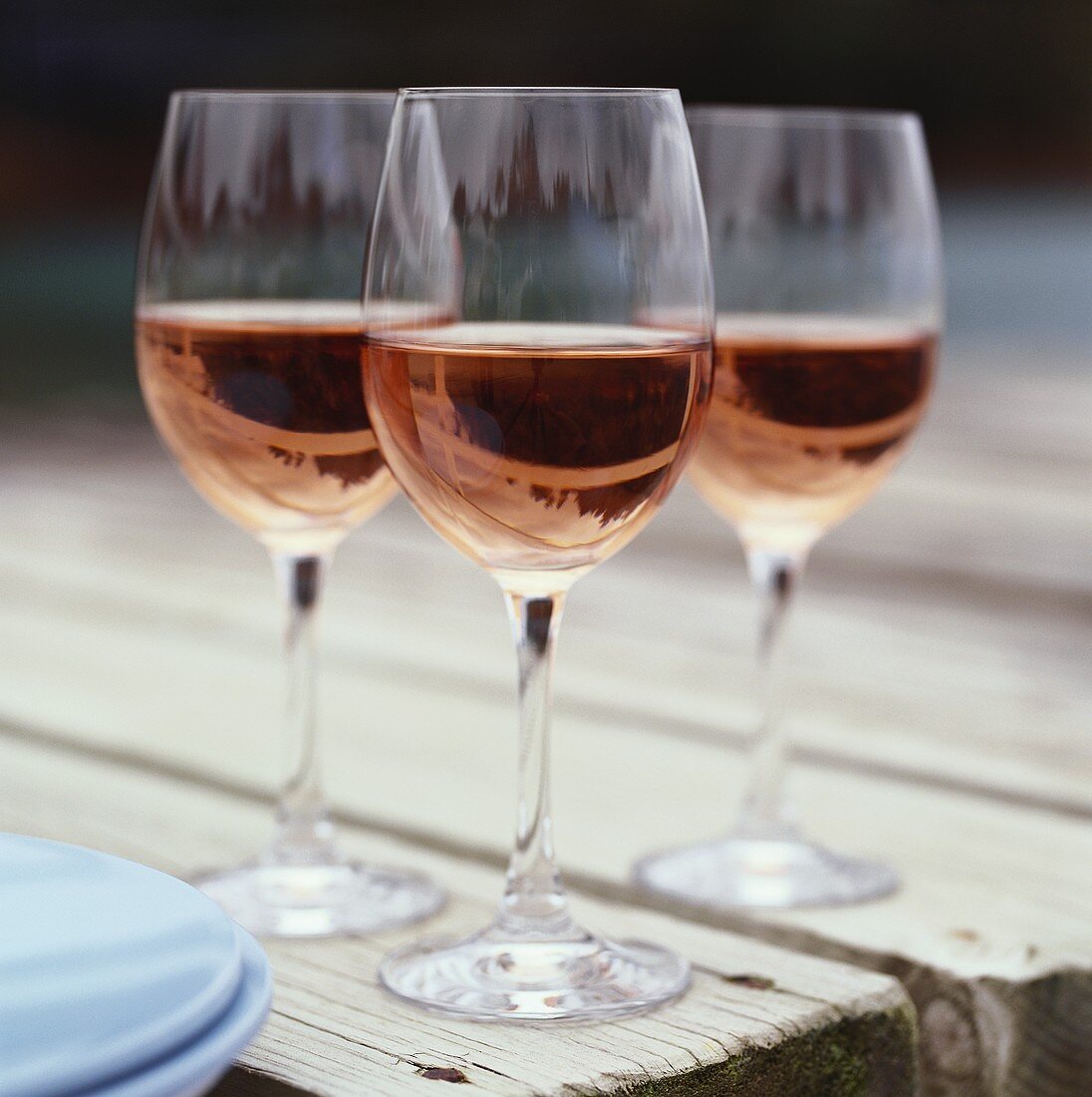 Three glasses of rosé wine on wooden table in the open air