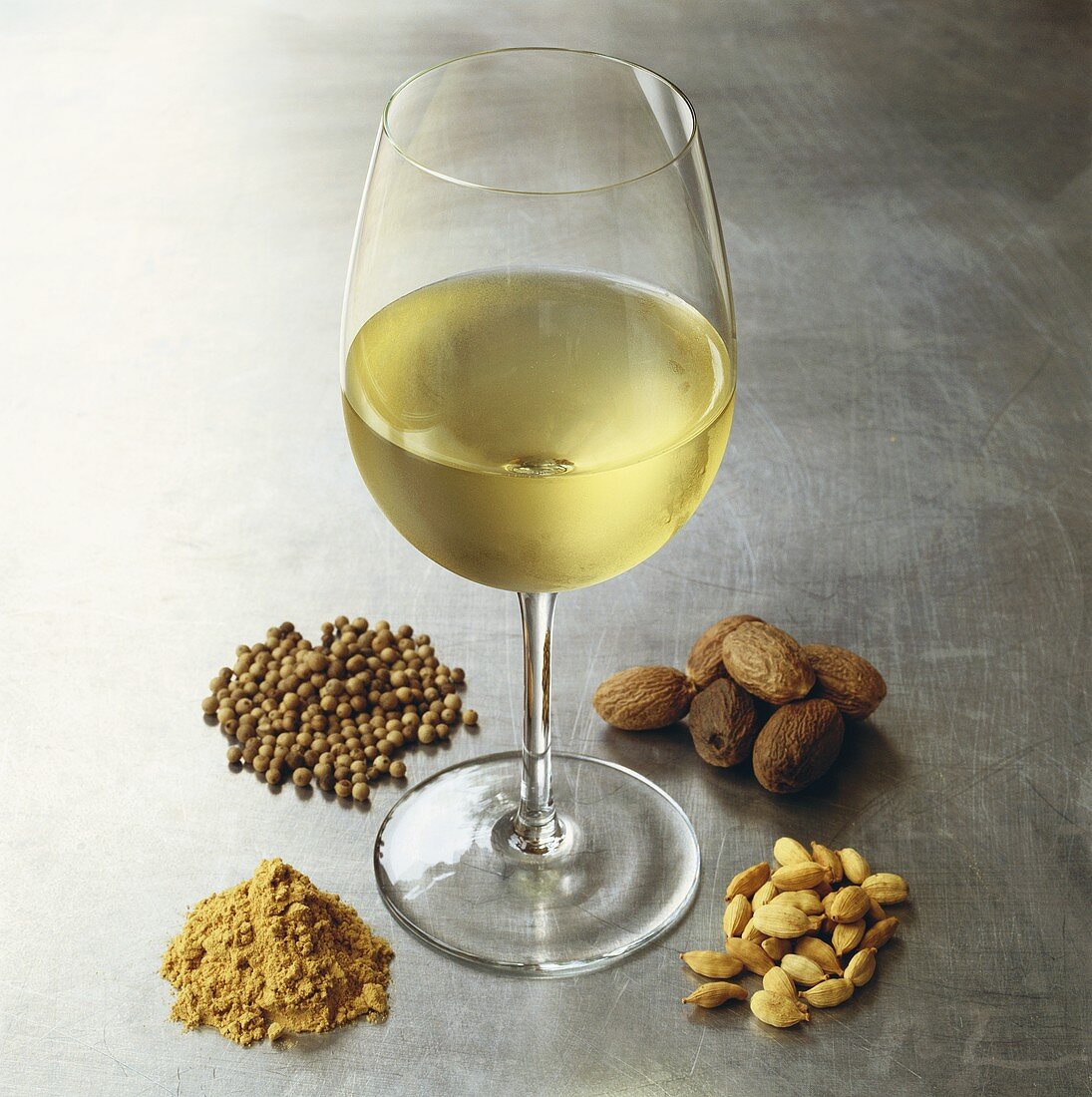 Glas Weißwein, umgeben von verschiedenen Gewürzen