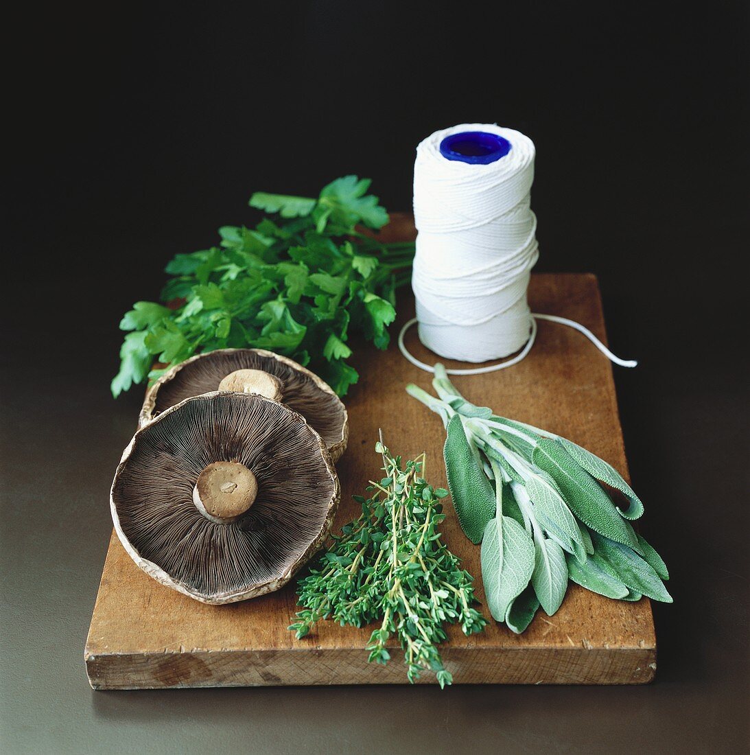 Mushrooms, fresh herbs & kitchen string on chopping board