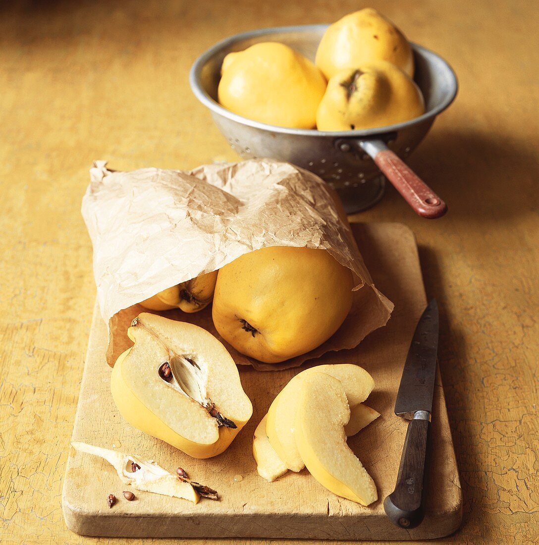 Quinces (whole and sliced) in paper bag on chopping board