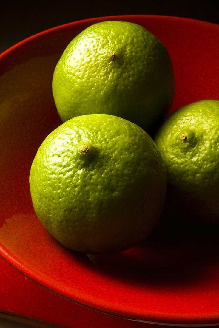 Three limes in a red bowl