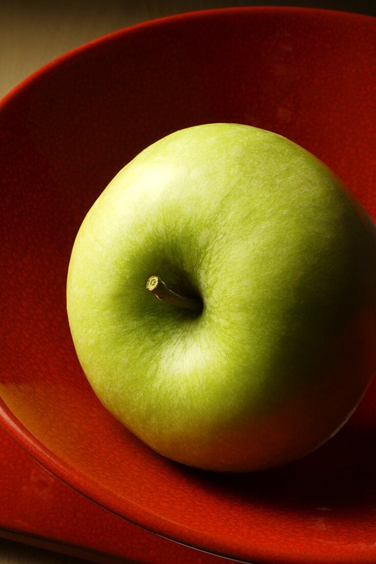 A Granny Smith apple in a red bowl