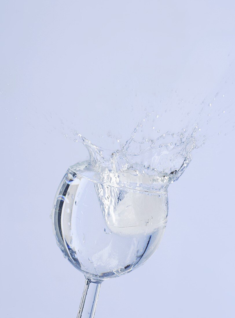 Eiswürfel fällt in Wasserglas