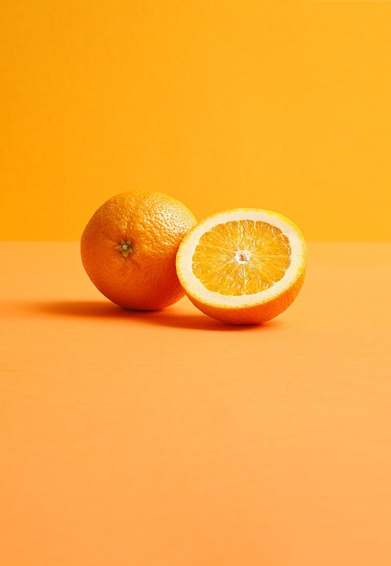 Ganze und halbe Orange auf orangefarbenem Hintergrund