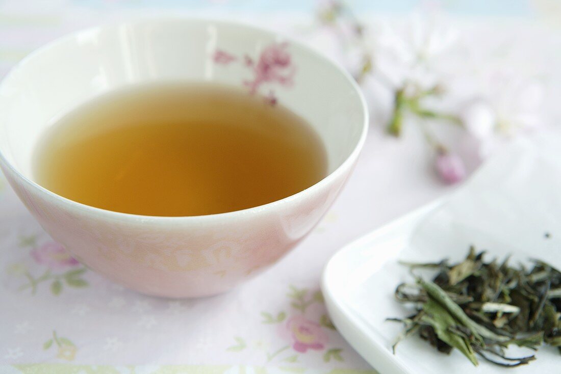 Tee in rosa Schale, Teeblätter und Kirschblüten