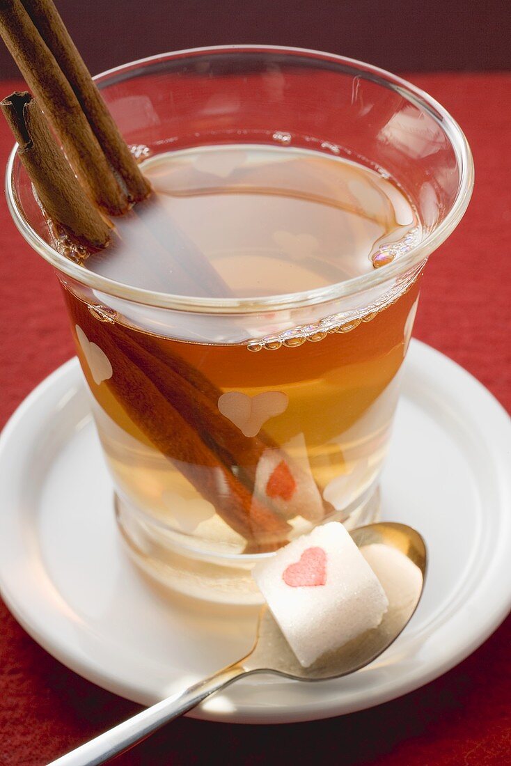 Glass of winter tea with cinnamon sticks, sugar cube on spoon