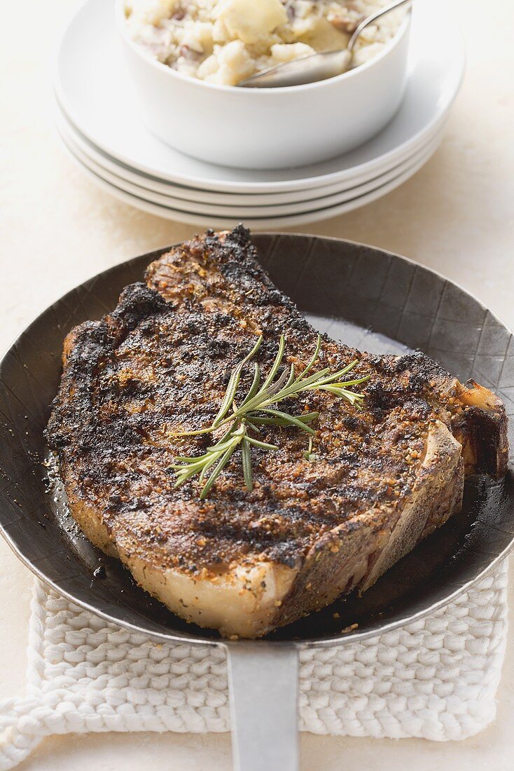 Rib eye steak in frying pan, mashed potatoes behind