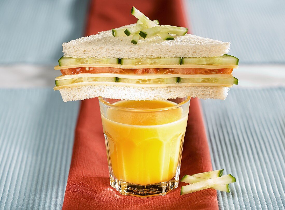 Tomato and cucumber tramezzini on a glass of orange juice