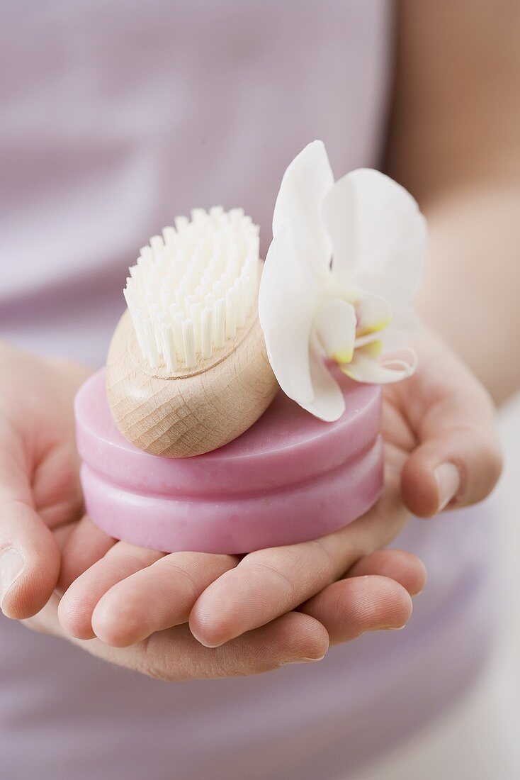 Woman holding soap, brush and orchid