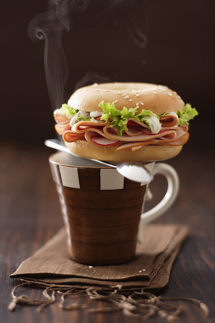Bagel filled with turkey ham on coffee cup