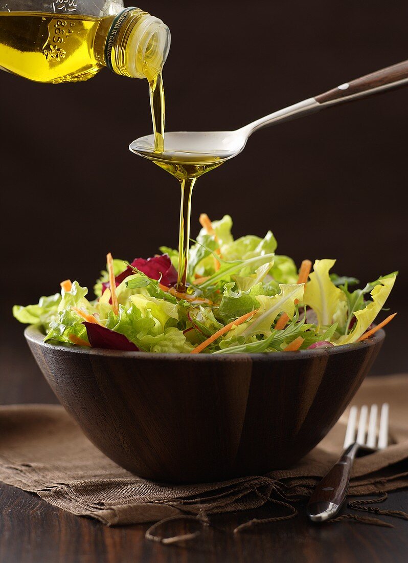 Olivenöl fliesst über Löffel auf gemischten Blattsalat