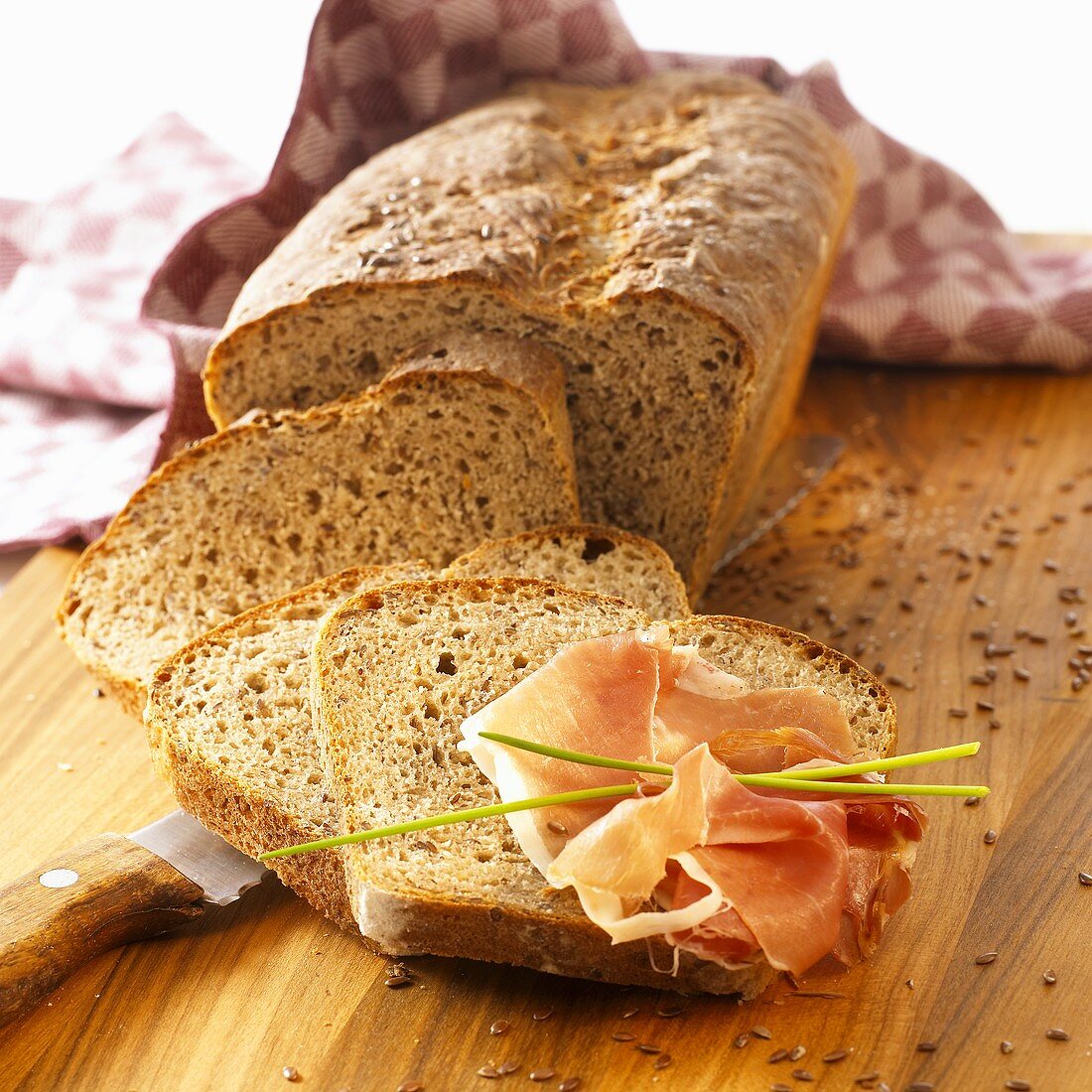 Linseed bread, partly sliced, raw ham on one slice