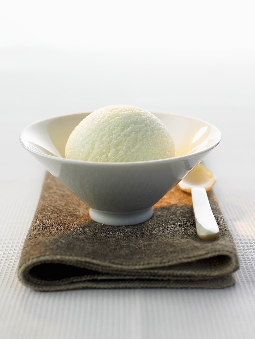 A scoop of tea ice cream in a bowl on brown cloth