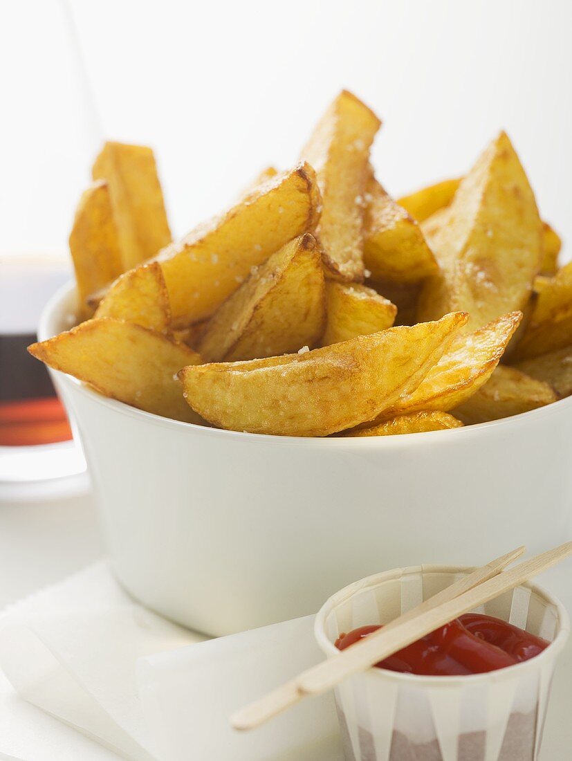 Potato wedges in white bowl, ketchup beside it