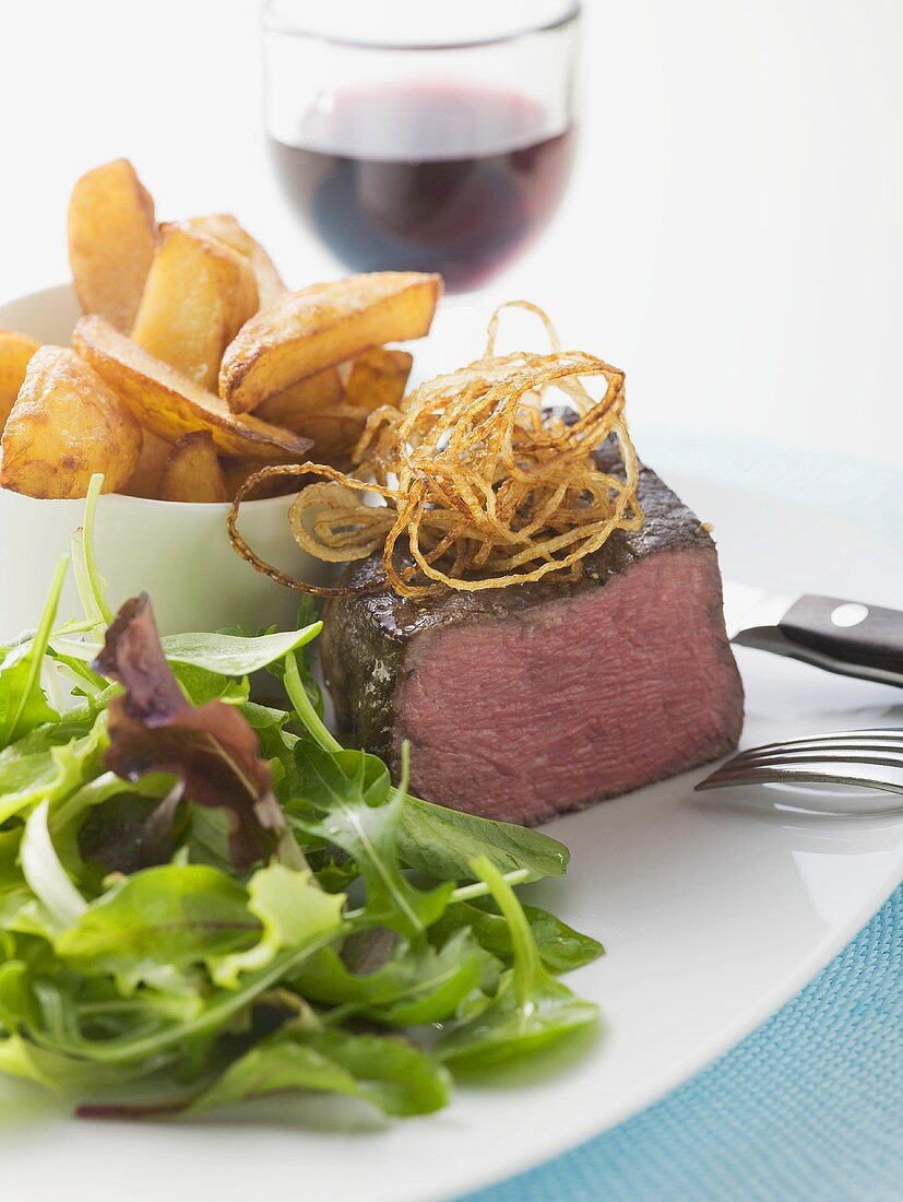 Beef fillet with salad leaves, potato wedges, glass of red wine