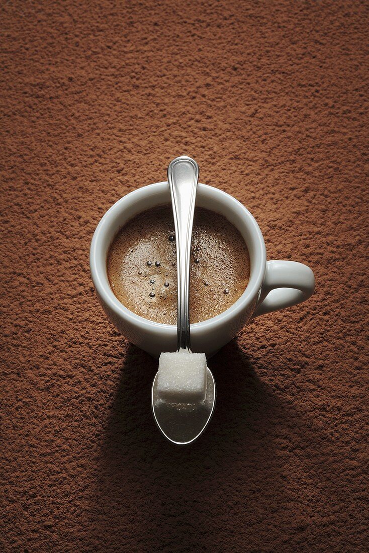 Espressotasse und Löffel mit Zuckerwürfel auf Kaffeepulver
