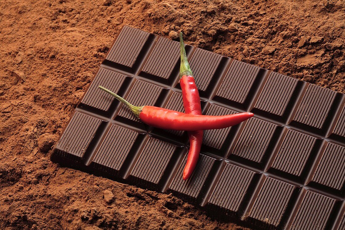 Schokoladentafel und zwei rote Chilischoten auf Kakaopulver