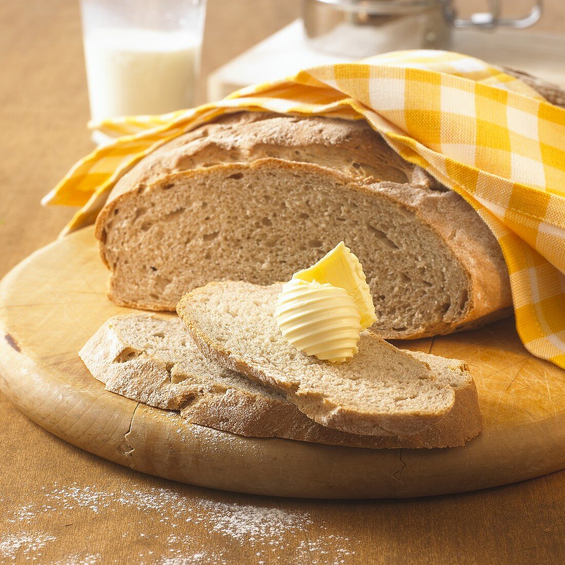 Farmhouse bread on wooden board, slice with butter curl