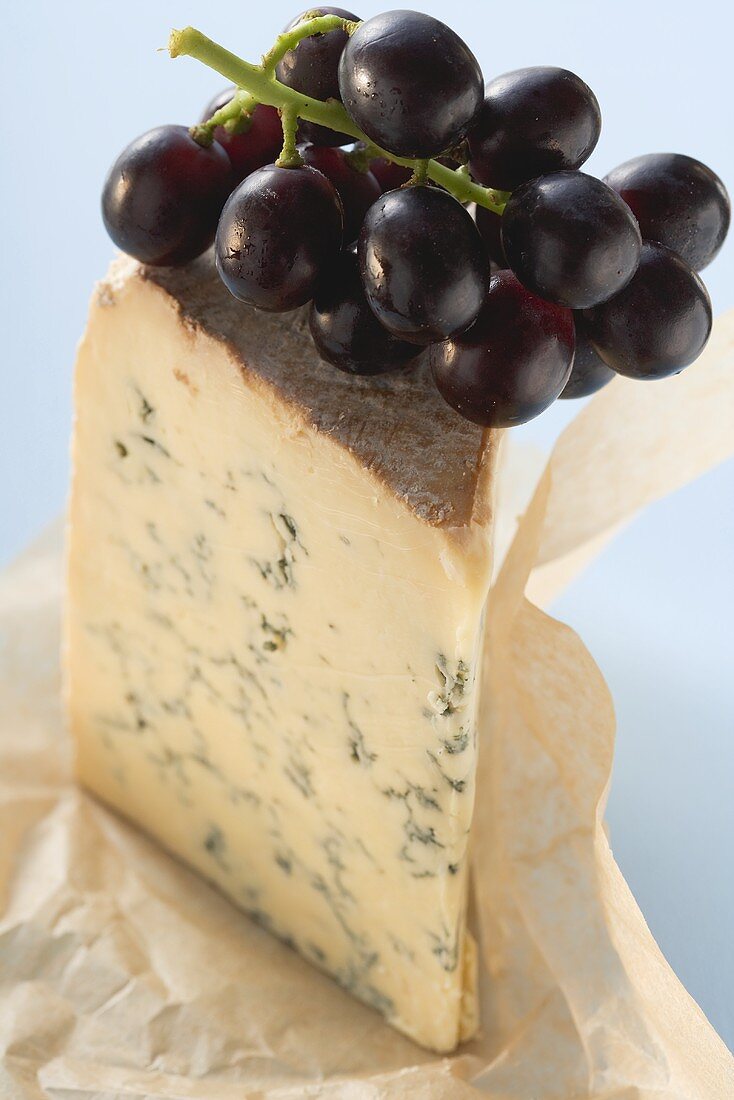 Piece of Stilton with red grapes on paper