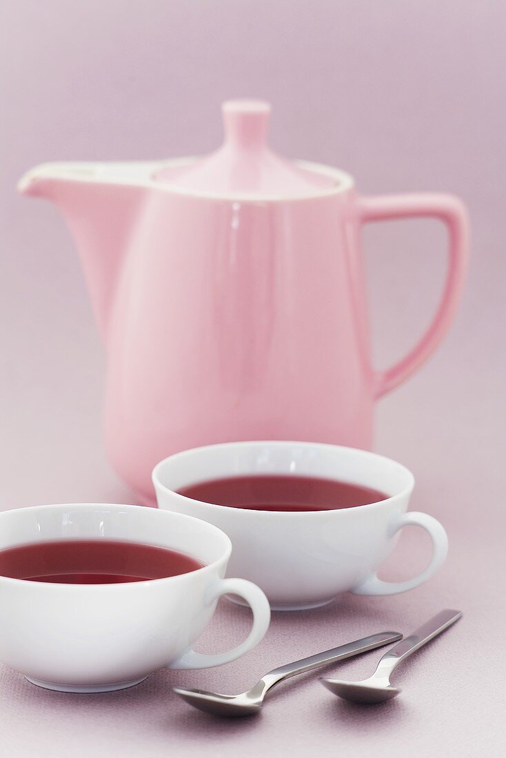 Zwei Tassen Früchtetee vor rosa Teekanne