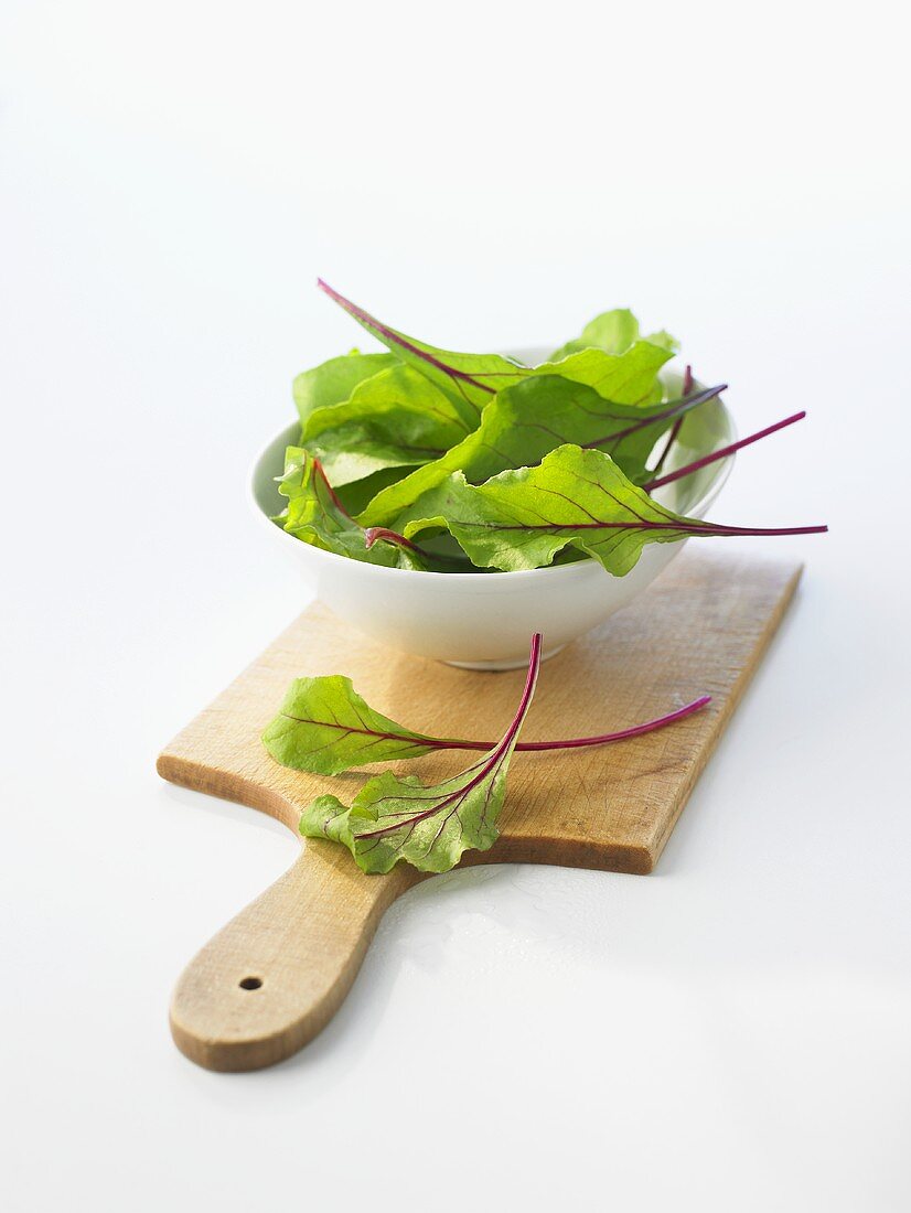 Young beetroot leaves in bowl on chopping board