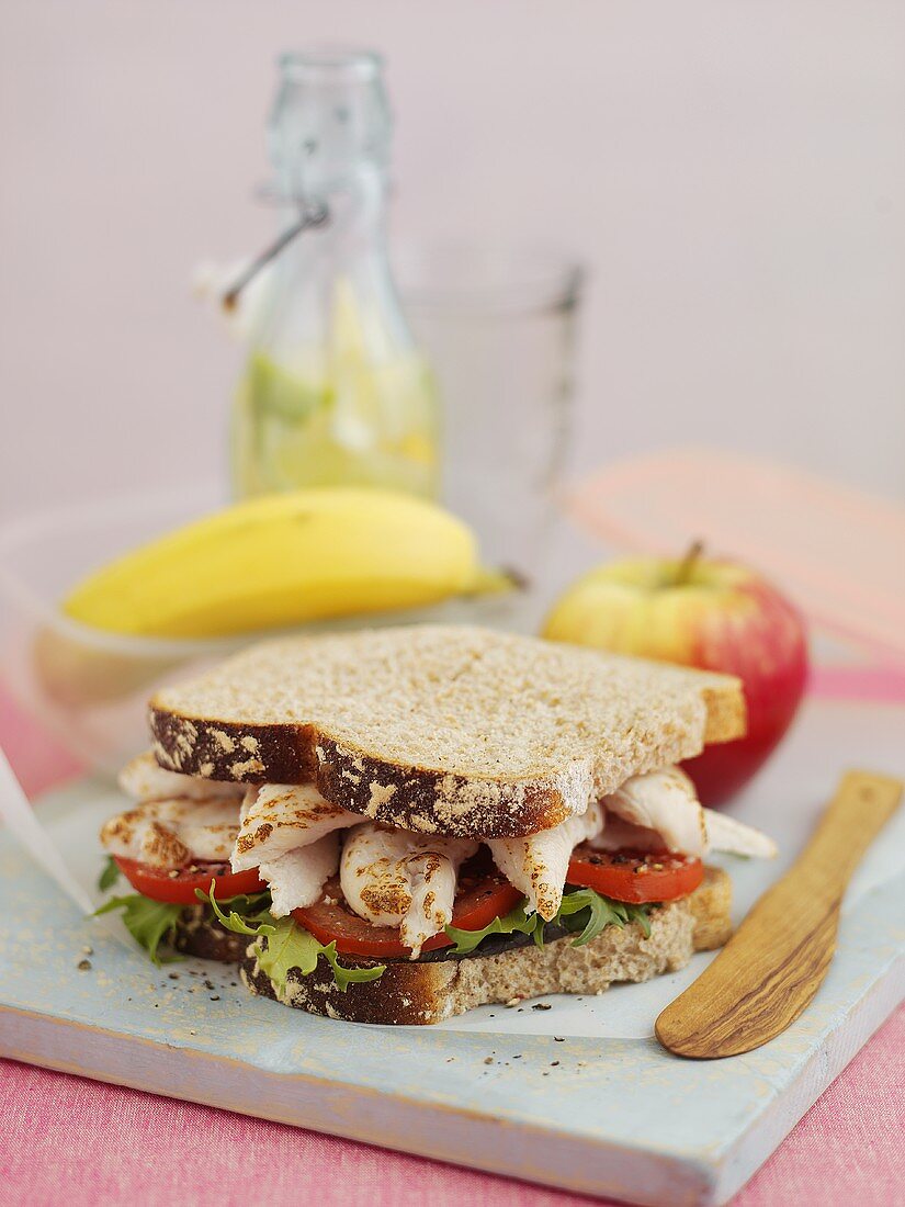 Sandwich mit Hähnchen, im Hintergrund Obst und Getränk