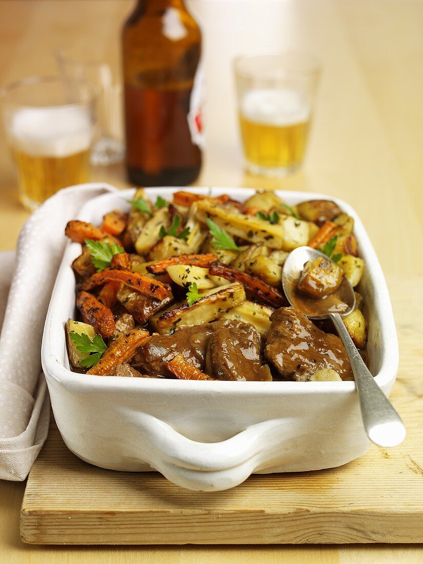 Beef & root vegetables in roasting dish, beer in background