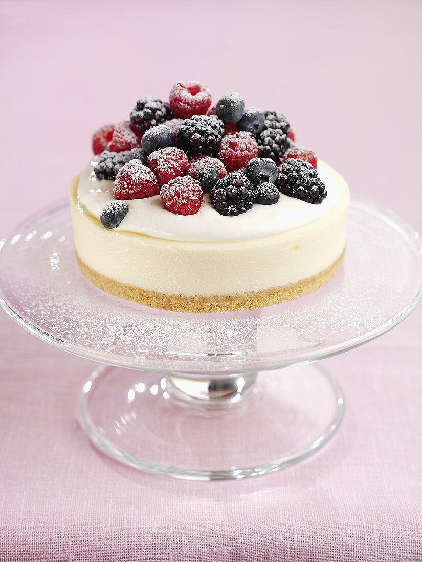 Käsesahnetorte mit Beeren und Puderzucker auf Tortenständer