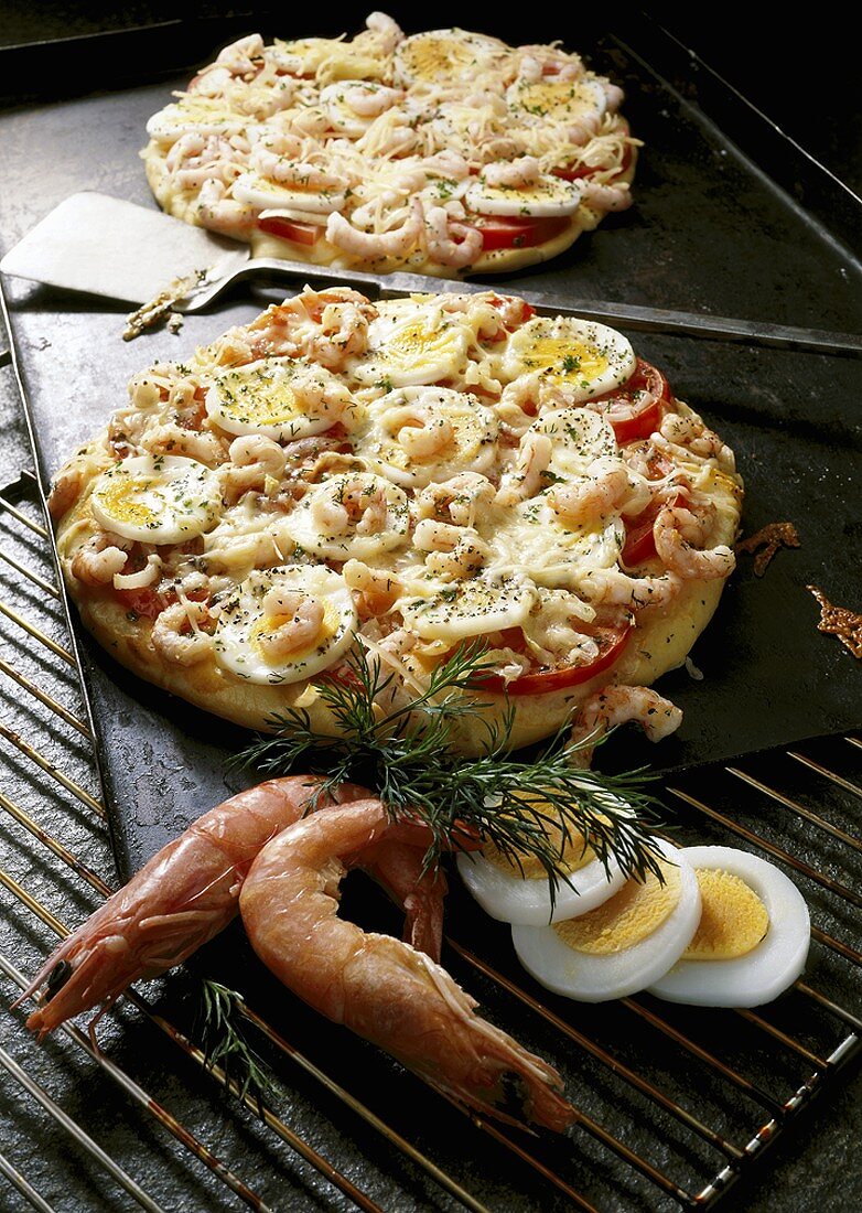 Zwei Pizzen mit Ei und Garnelen auf Backblech