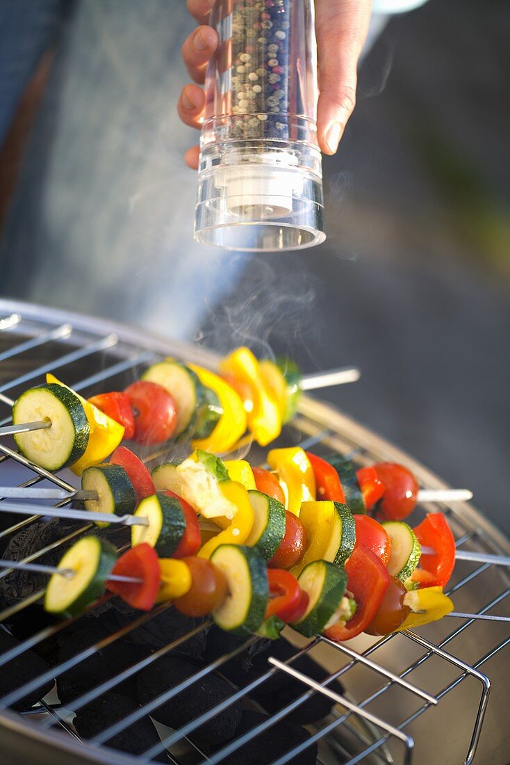 Vegetable kebabs on barbecue being sprinkled with pepper