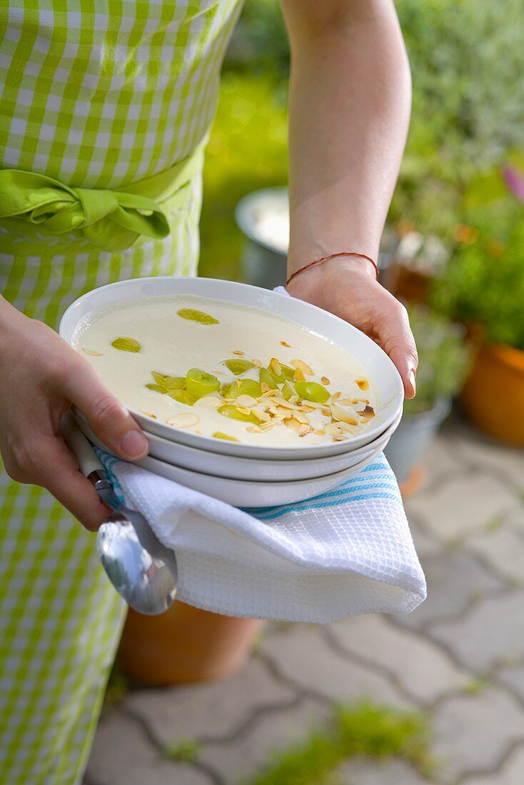Woman holding plate of gazpacho blanco (cold almond soup, Spain)