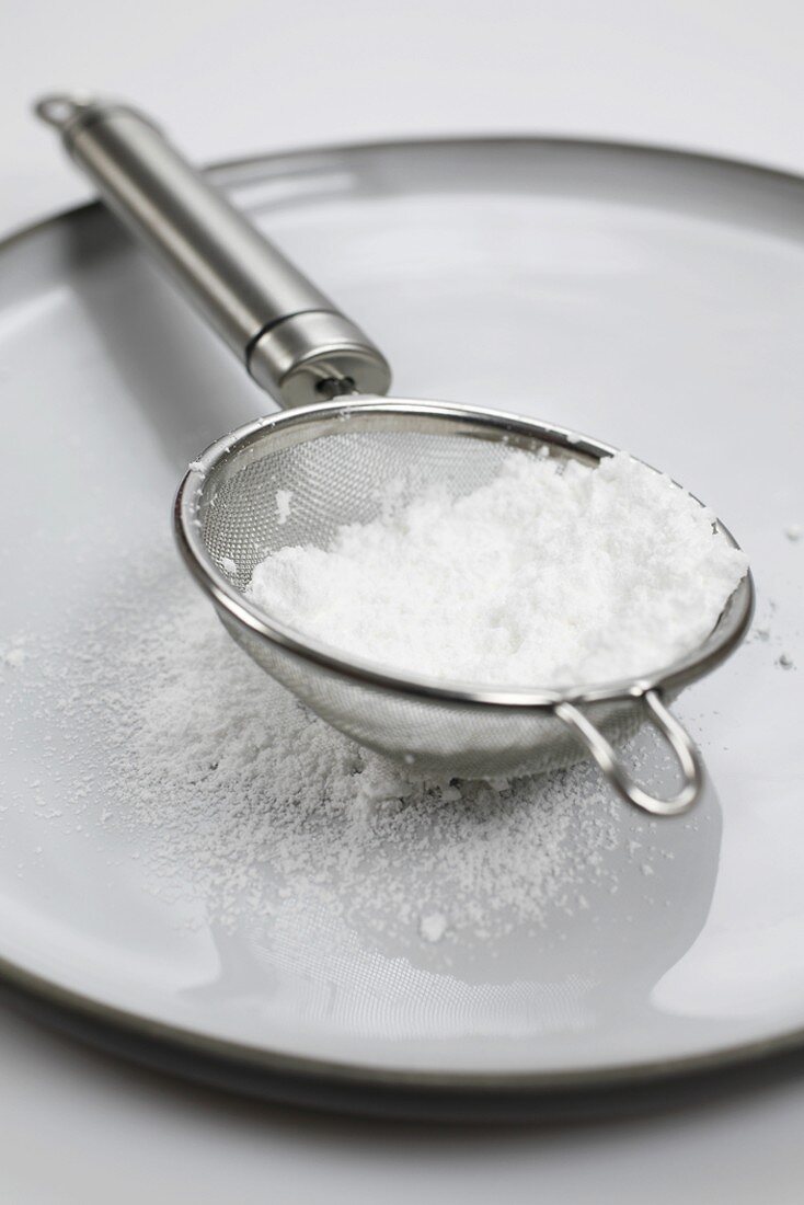 Icing sugar in sieve on grey plate