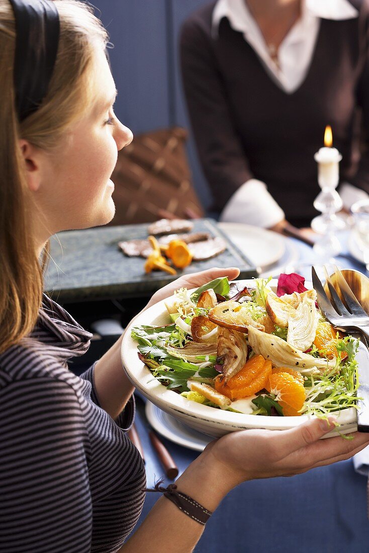 A young woman holding a plate of bread salad with fennel and mandarins