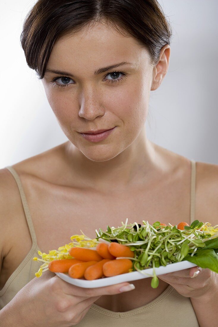 Young woman holding plate of raw vegetable salad
