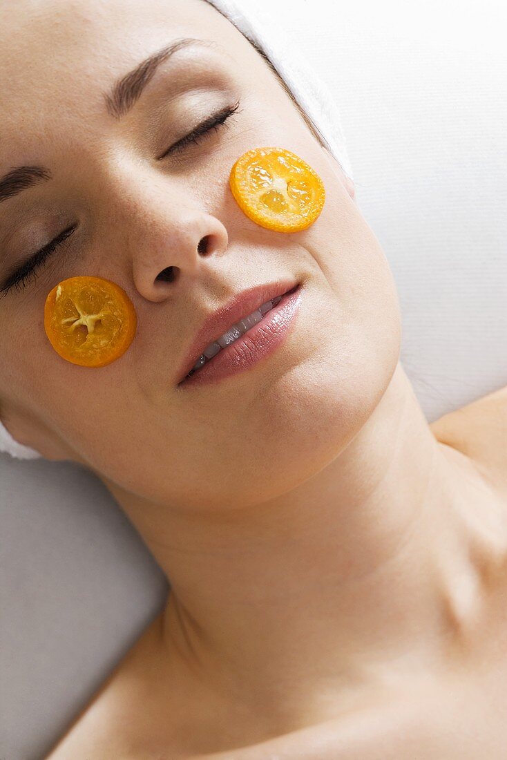 Young woman with slices of kumquat in front of her face