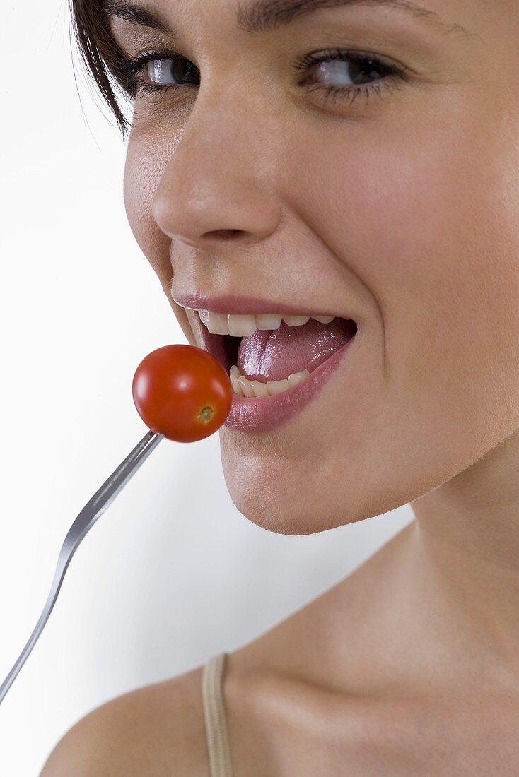 Young woman eating a cocktail tomato (close-up)