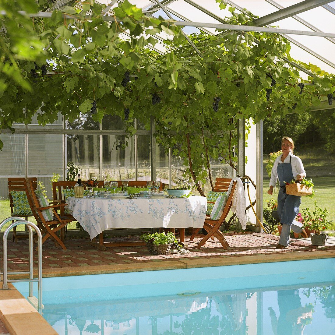 Laid table by pool and young woman wearing gardening apron